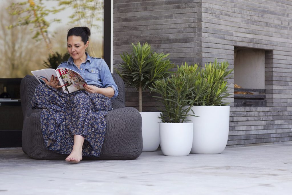 vrouw die in de tuin een tijdschrift aan het lezen is met capi bloempotten op de achtergrond